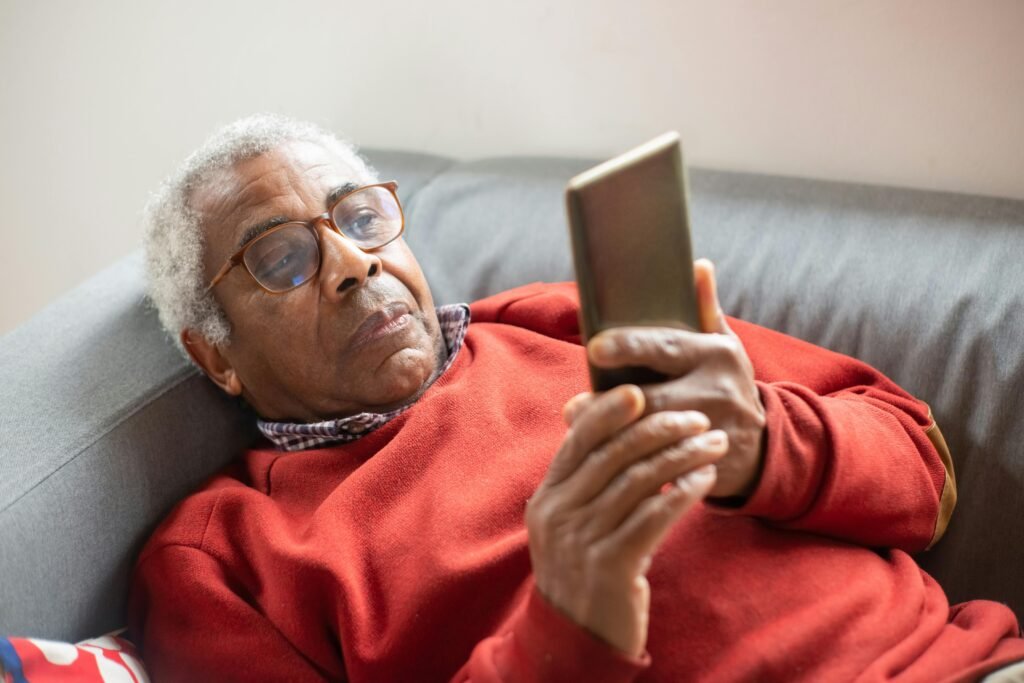 A senior male laying on a couch viewing an android smartphone 